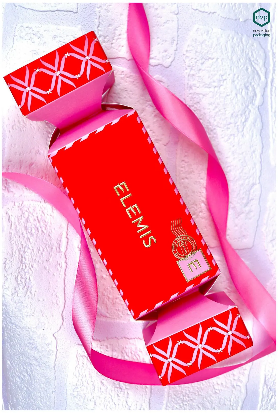 Red Elemis cracker carton with foil-blocked lettering and a printed pattern, laid on a pink ribbon