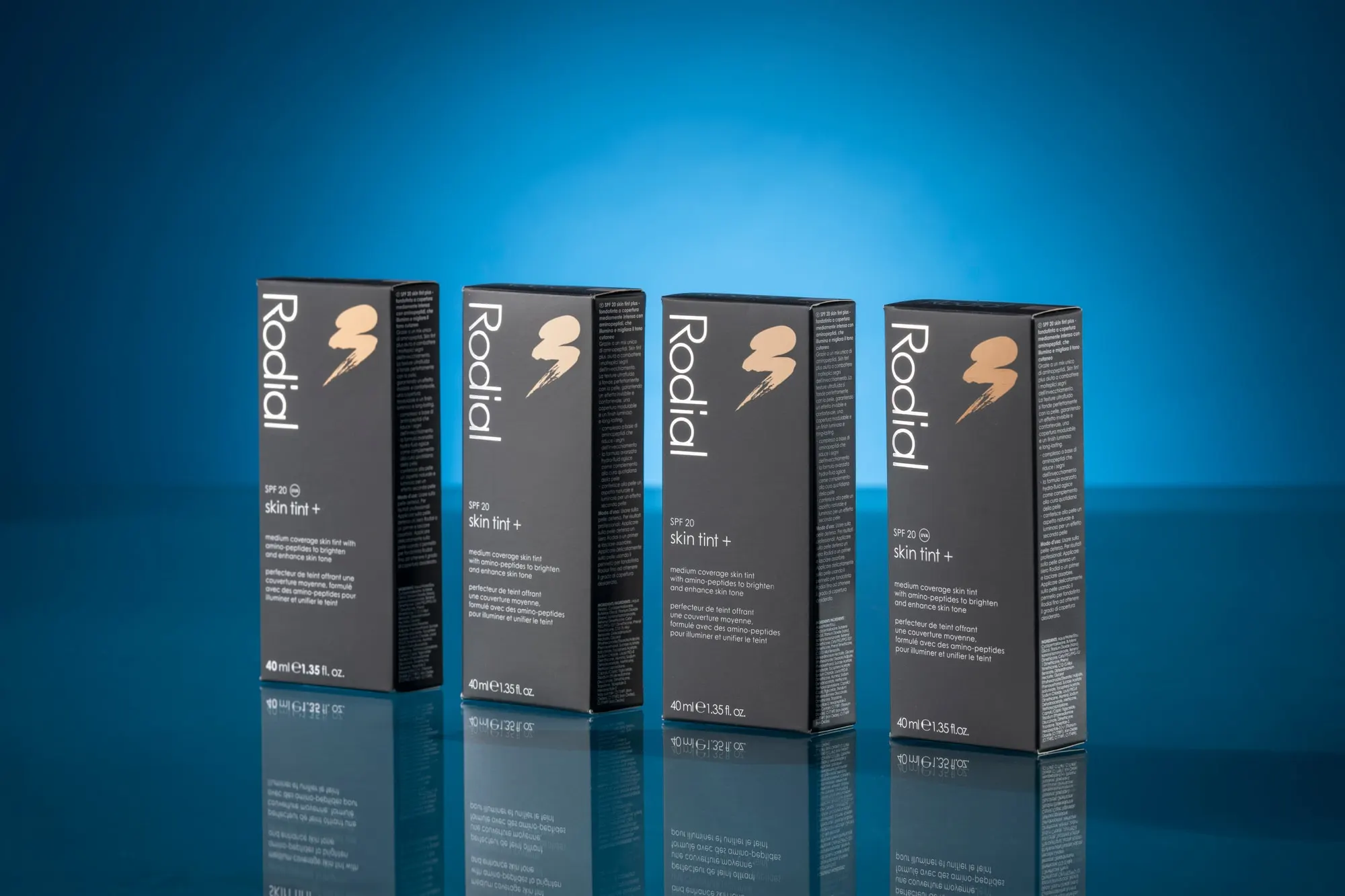 Four black Rodial skin tint cartons with foil-blocked lightning marks, on a blue reflective ground