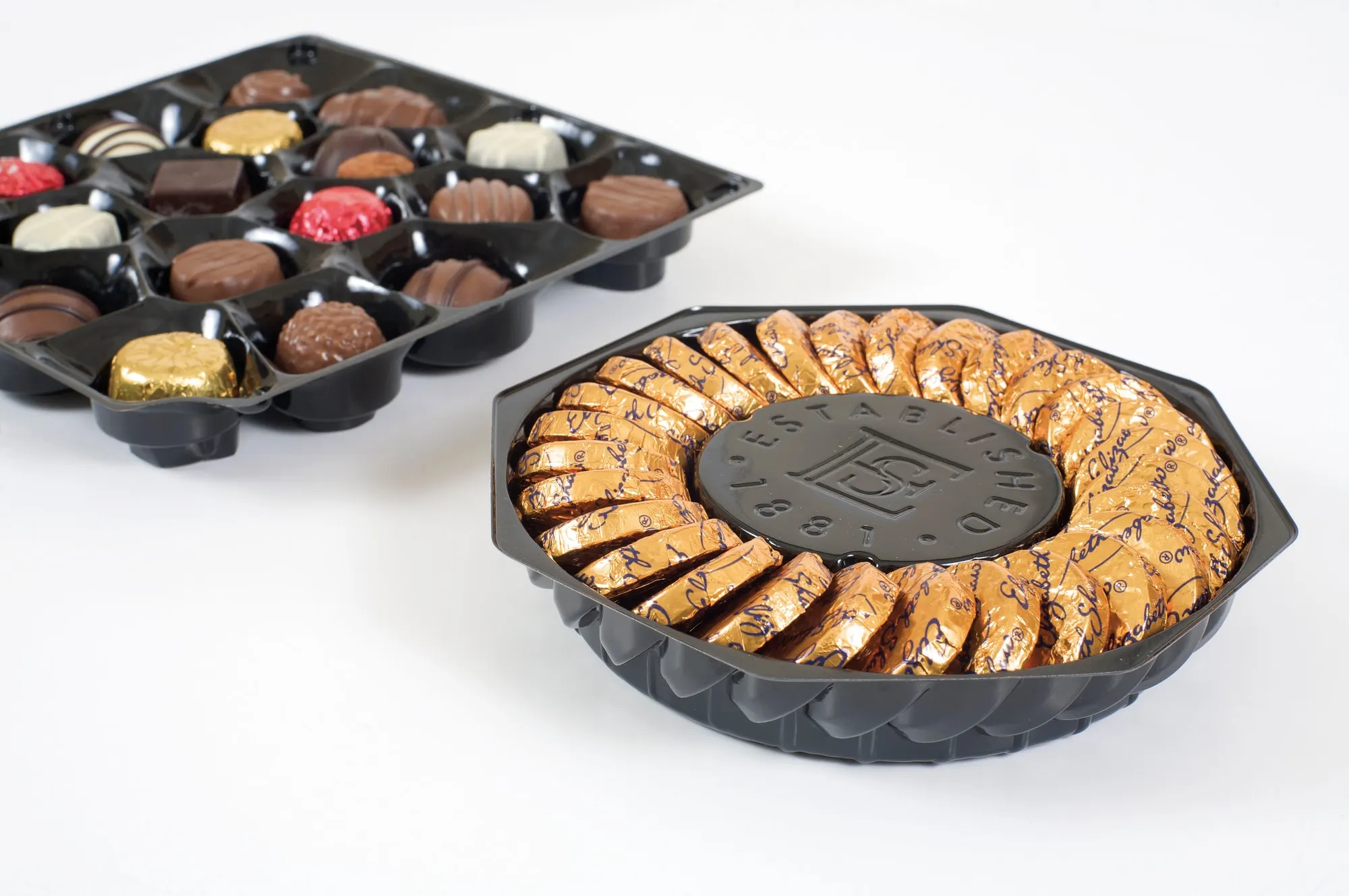 A rectangular vacuum formed chocolate tray beside a round scalloped tray holding a caramel tart