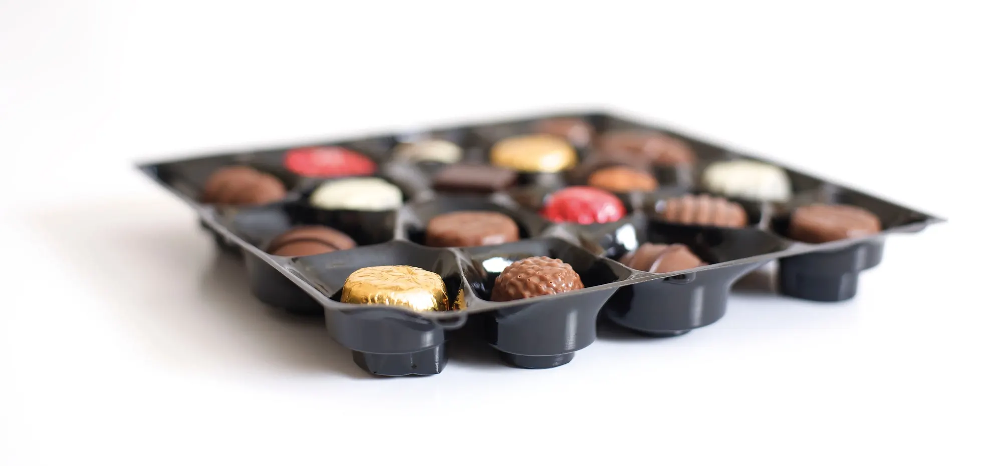 Black vacuum formed tray with individual cavities holding a mixed chocolate selection